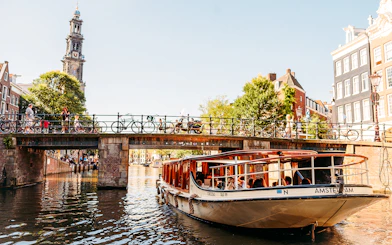 Amsterdam canal cruise boat passing under a bridge with Westerkerk tower in the background.
