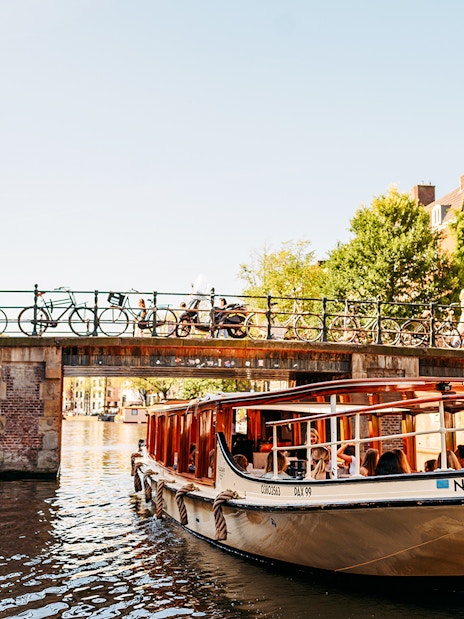 Amsterdam canal cruise boat passing under a bridge with Westerkerk tower in the background.