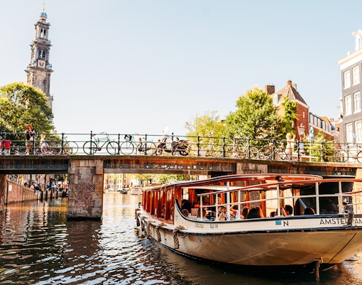 Amsterdam canal cruise boat passing under a bridge with Westerkerk tower in the background.