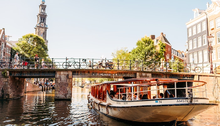 Amsterdam canal cruise boat passing under a bridge with Westerkerk tower in the background.