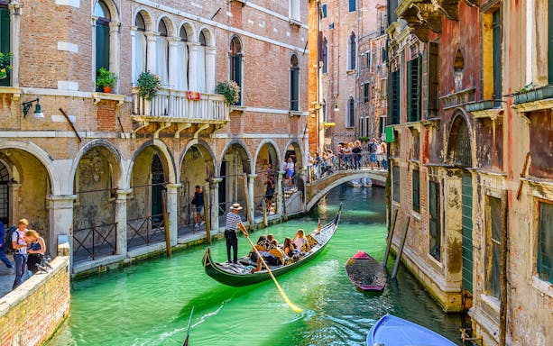 Gondola navigating a narrow canal under a bridge in Venice, Italy.