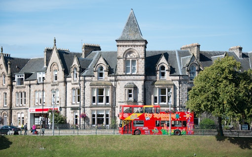 Red double-decker sightseeing bus in front of historic Inverness building on 24-Hr Hop-On Hop-Off Tour.