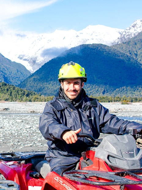 Two people quad biking with snowy mountains at Franz Josef, New Zealand.