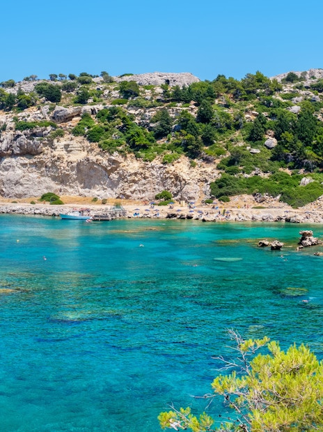 Sailboat in turquoise waters of Anthony Quinn Bay, Rhodes, Greece, with rocky cliffs and beach.