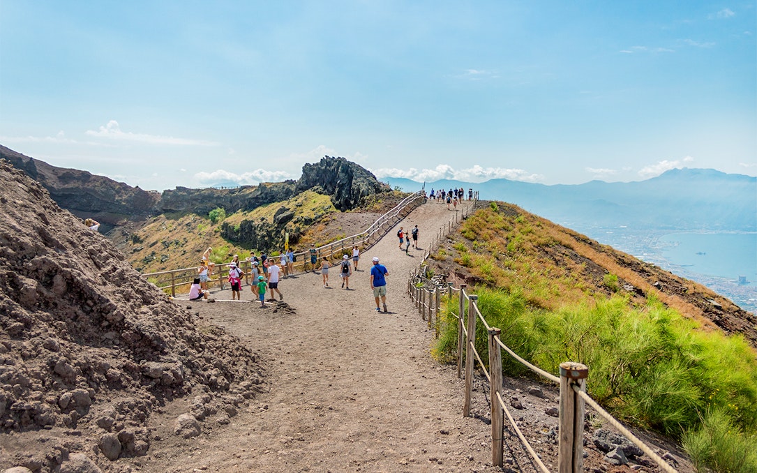 Hikers walking on a trail along Mount Vesuvius with a view of the surrounding landscape.