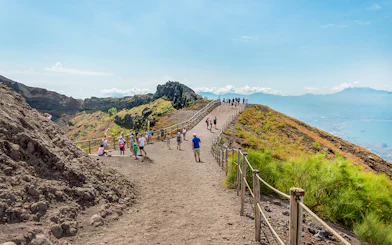 Hikers walking on a trail along Mount Vesuvius with a view of the surrounding landscape.