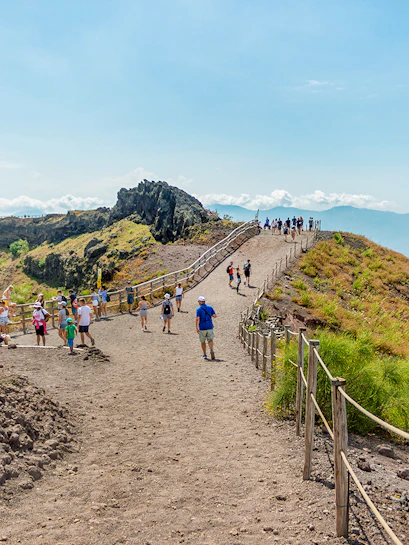 Hikers walking on a trail along Mount Vesuvius with a view of the surrounding landscape.