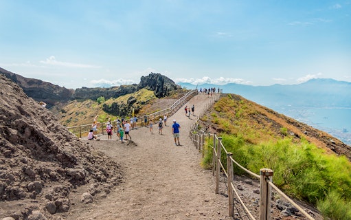 Hikers walking on a trail along Mount Vesuvius with a view of the surrounding landscape.