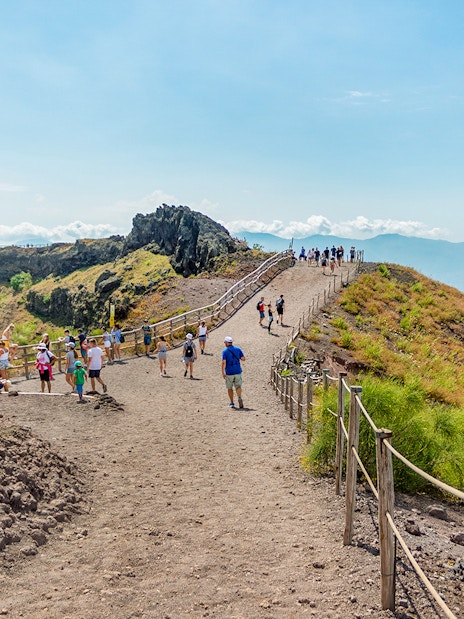 Hikers walking on a trail along Mount Vesuvius with a view of the surrounding landscape.