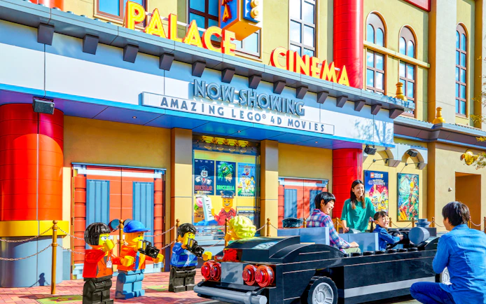 Family enjoying Lego car ride at Legoland Japan's Palace Cinema entrance.