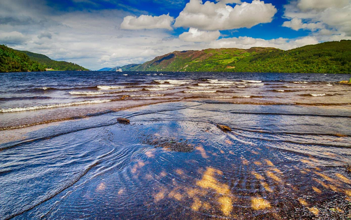 Loch Ness shoreline with distant hills and a boat on the water.