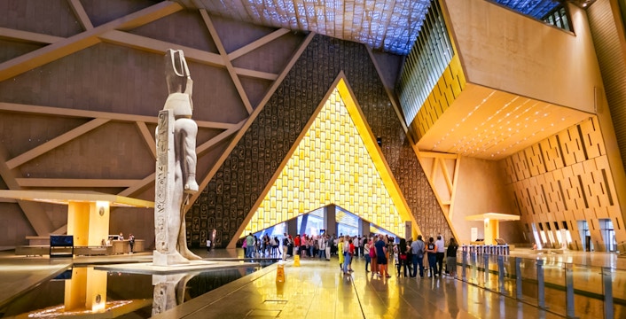 Visitors exploring the Grand Egyptian Museum interior with large statue and modern architecture.