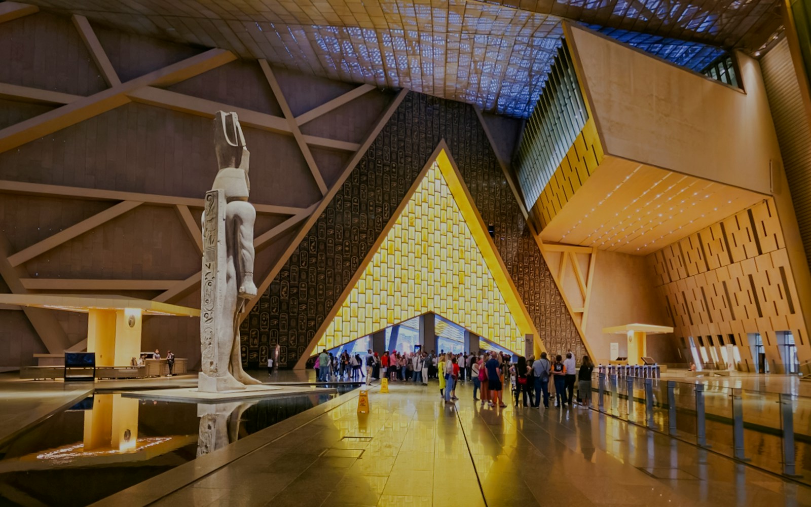 Visitors exploring the Grand Egyptian Museum interior with large statue and modern architecture.