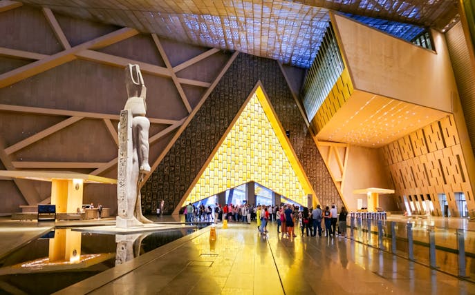 Visitors exploring the Grand Egyptian Museum interior with large statue and modern architecture.