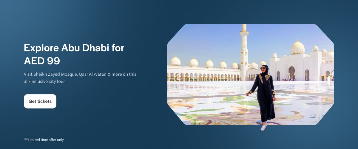 Sheikh Zayed Mosque in Abu Dhabi with a visitor walking on the marble courtyard.