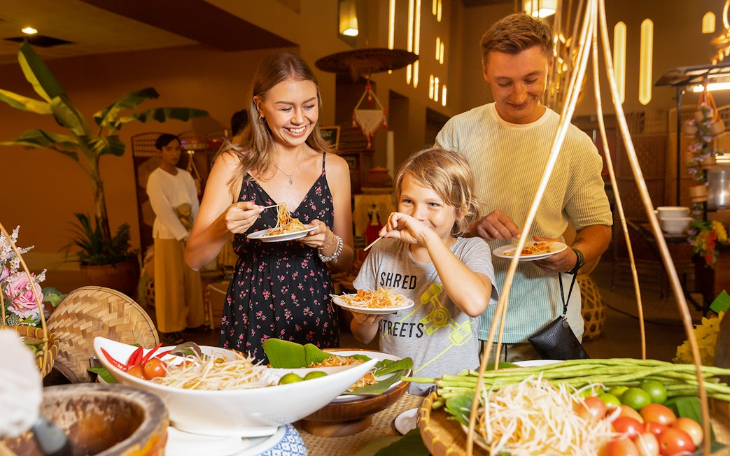 Family enjoying buffet dinner at Siam Niramit with plates of noodles and fresh vegetables.