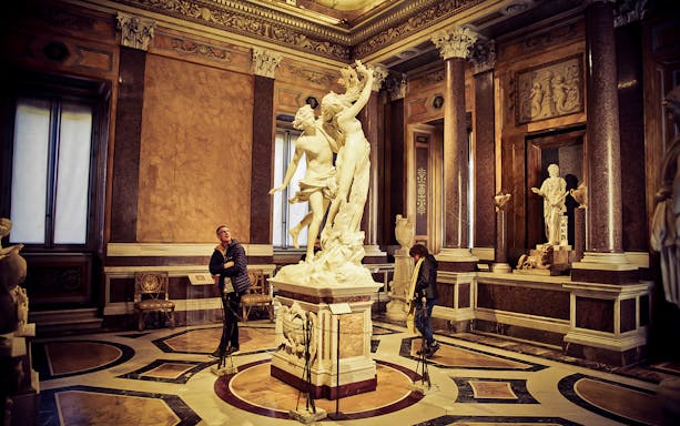 Borghese Gallery visitors admire sculptures in an ornate room, Rome.