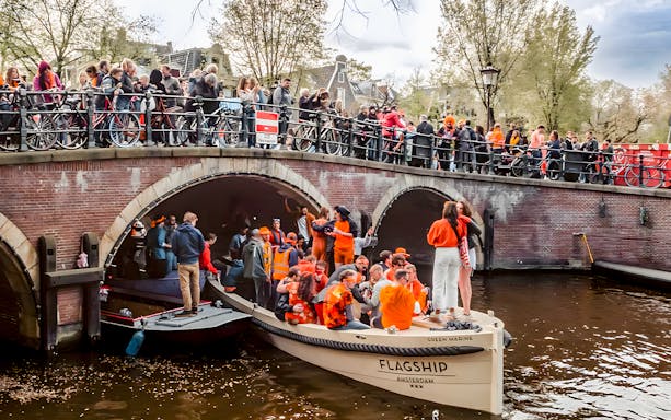 Amsterdam canal boat with people celebrating King's Day in orange attire.