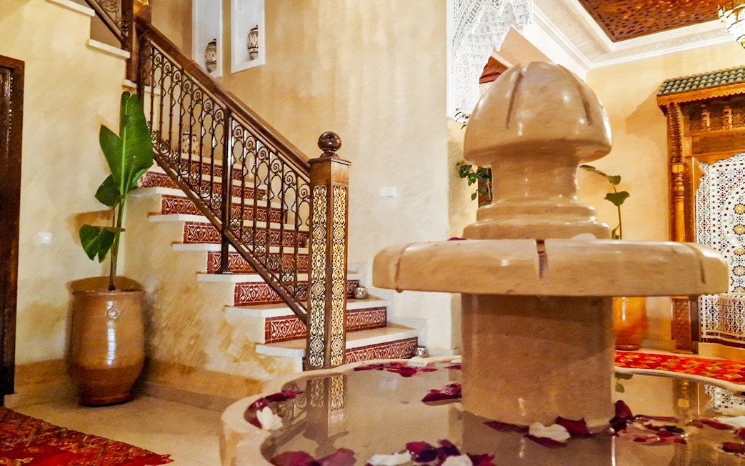 Traditional Moroccan hammam interior with ornate staircase and decorative fountain.