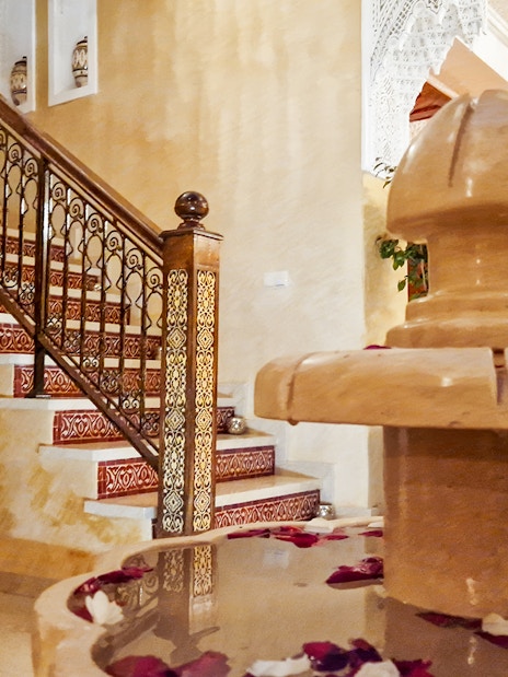 Traditional Moroccan hammam interior with ornate staircase and decorative fountain.