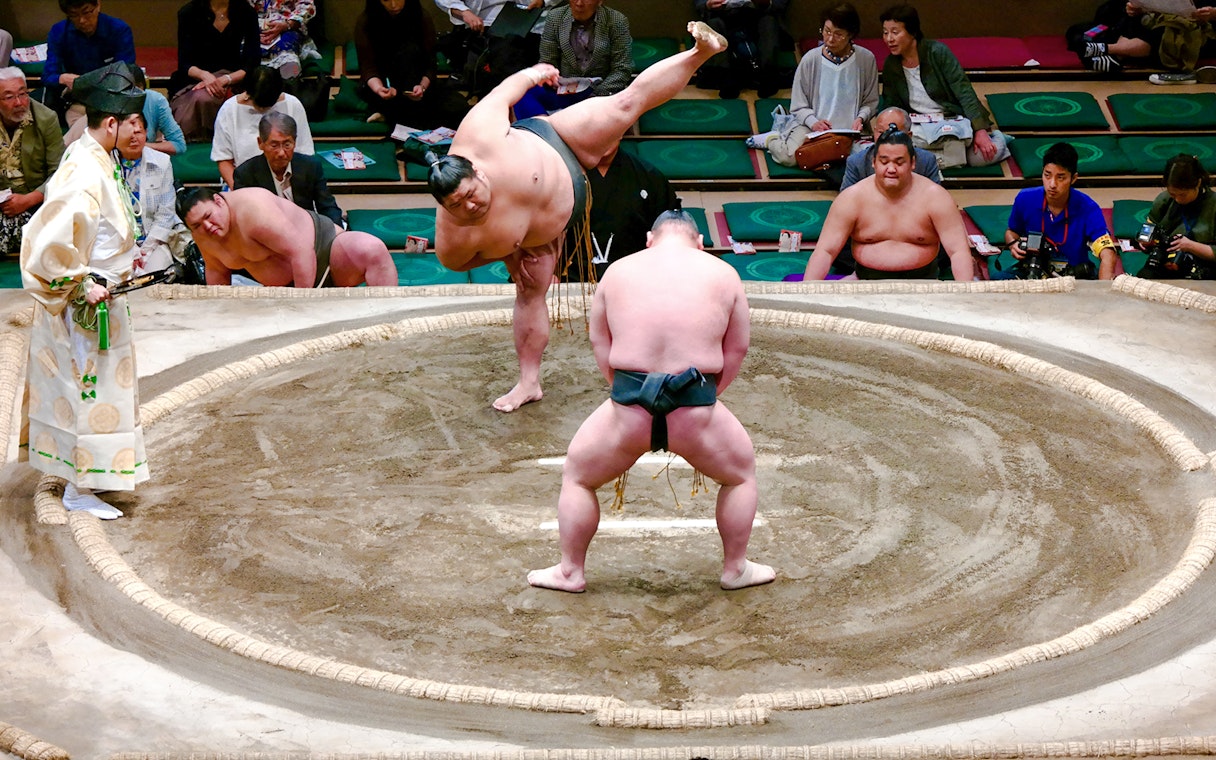 Sumo wrestlers compete on the dohyo, surrounded by an audience.
