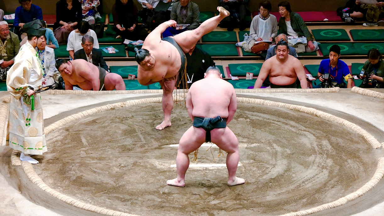 Sumo wrestlers compete on the dohyo, surrounded by an audience.