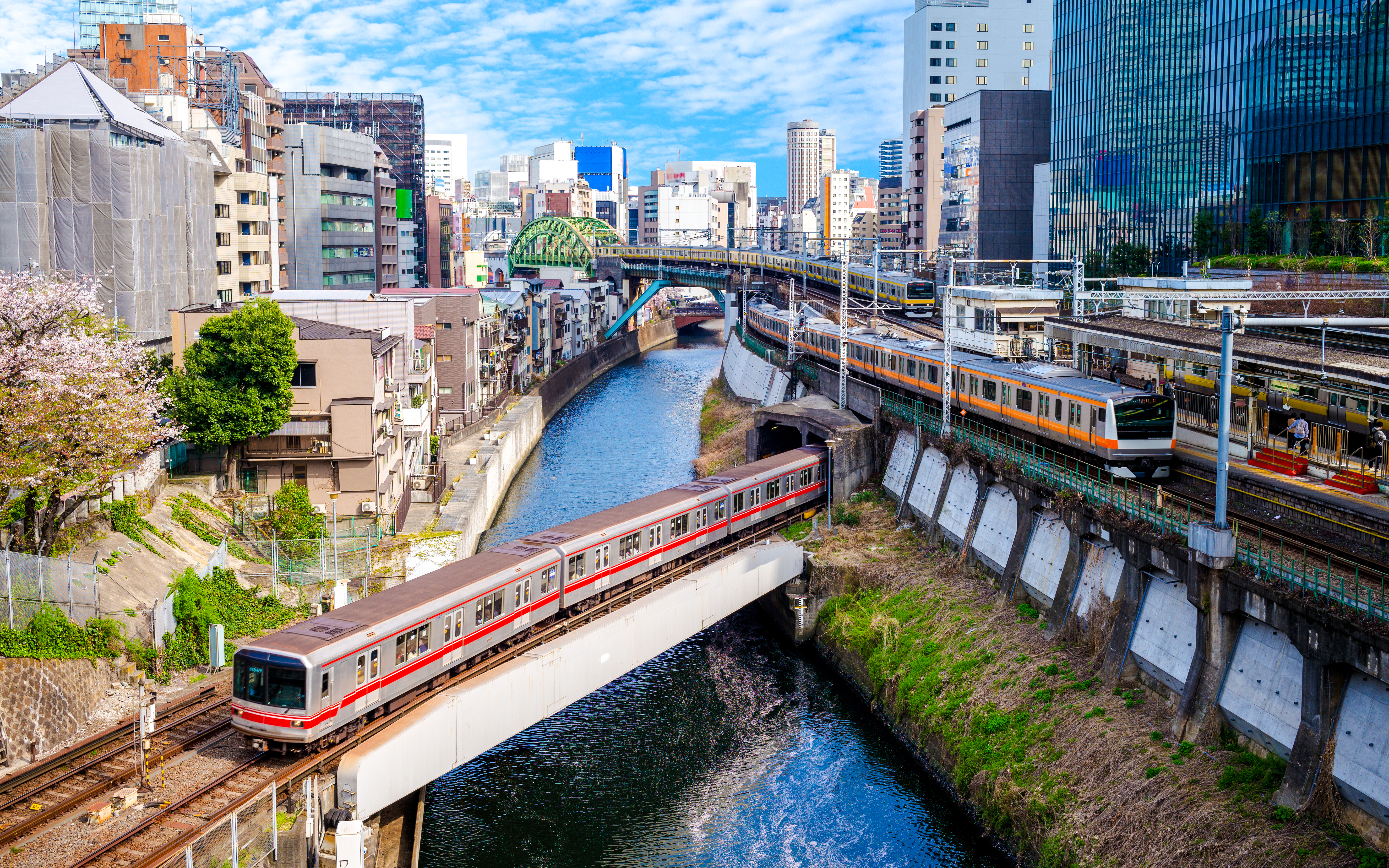 Tokyo metro trains crossing a river with cityscape in the background.
