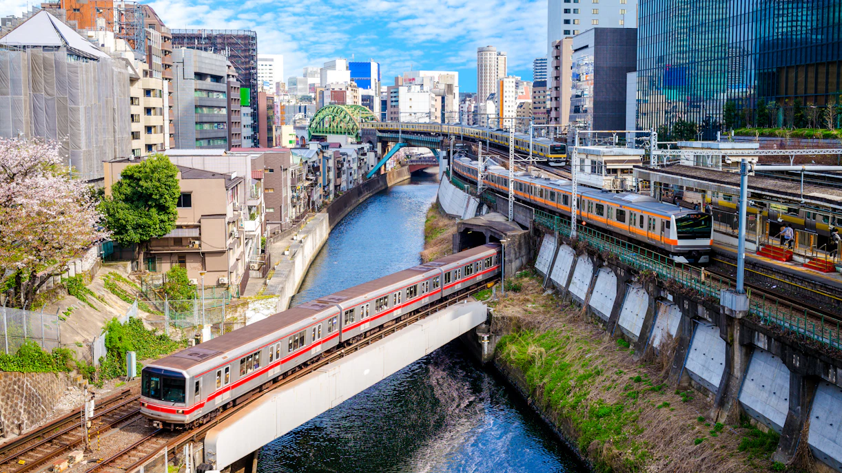 Tokyo metro trains crossing a river with cityscape in the background.