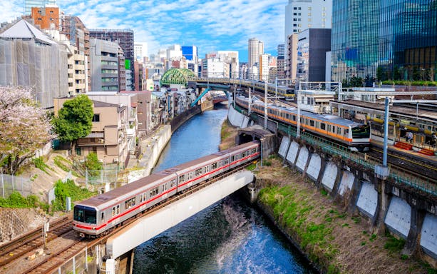 Tokyo metro trains crossing a river with cityscape in the background.