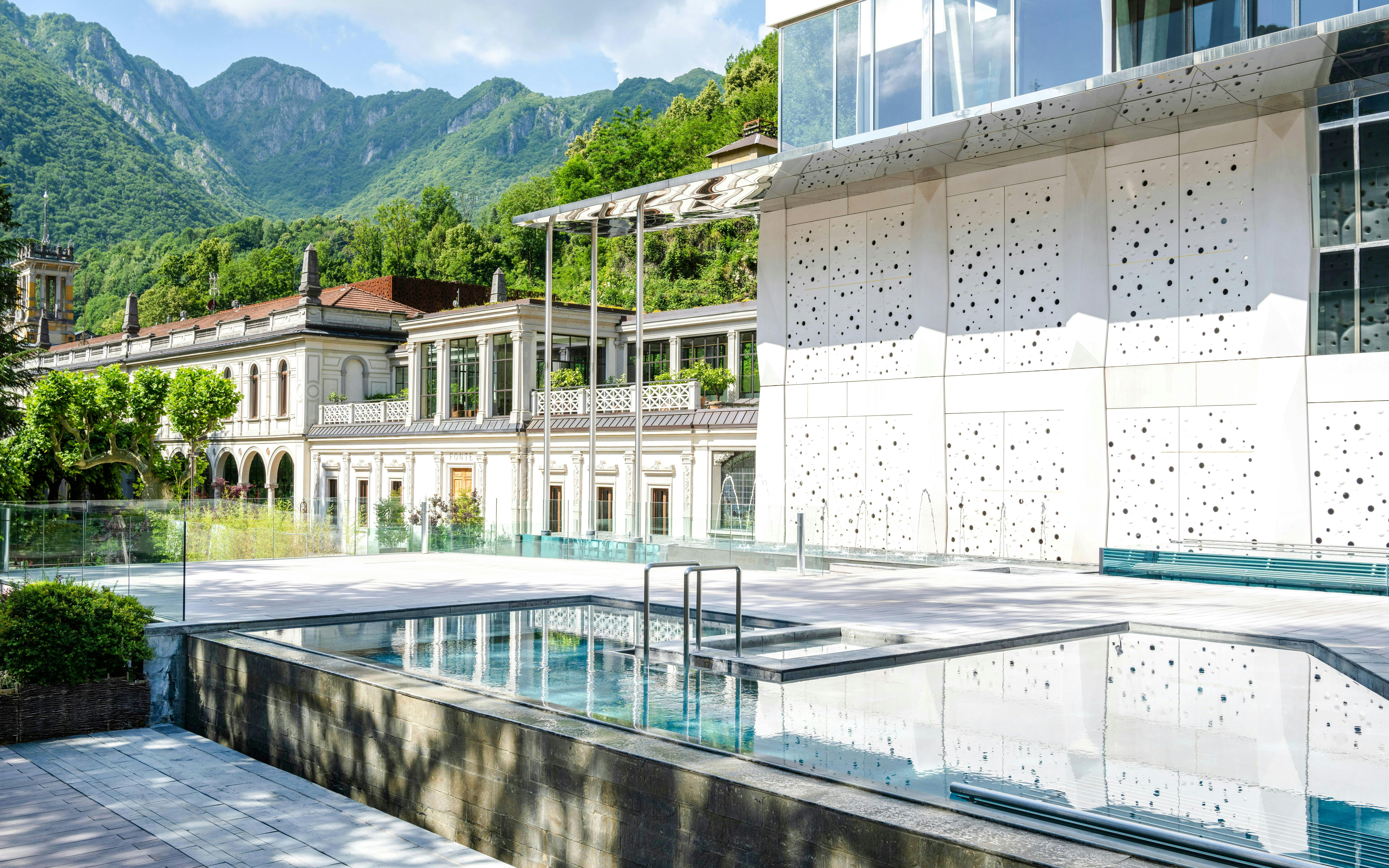 Outdoor pool area at QC Terme San Pellegrino Spa with mountain backdrop.