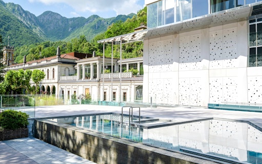 Outdoor pool area at QC Terme San Pellegrino Spa with mountain backdrop.