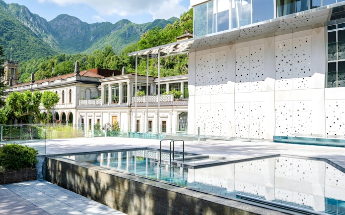 Outdoor pool area at QC Terme San Pellegrino Spa with mountain backdrop.