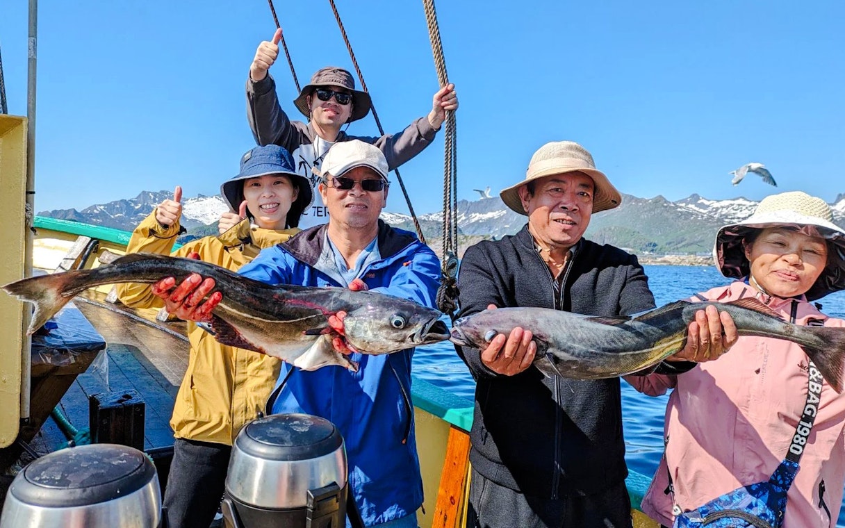 Guests holding pollock on a fishing boat cruise in Lofoten, with mountains in the background.