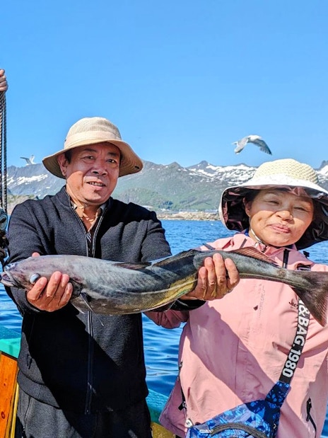 Guests holding pollock on a fishing boat cruise in Lofoten, with mountains in the background.