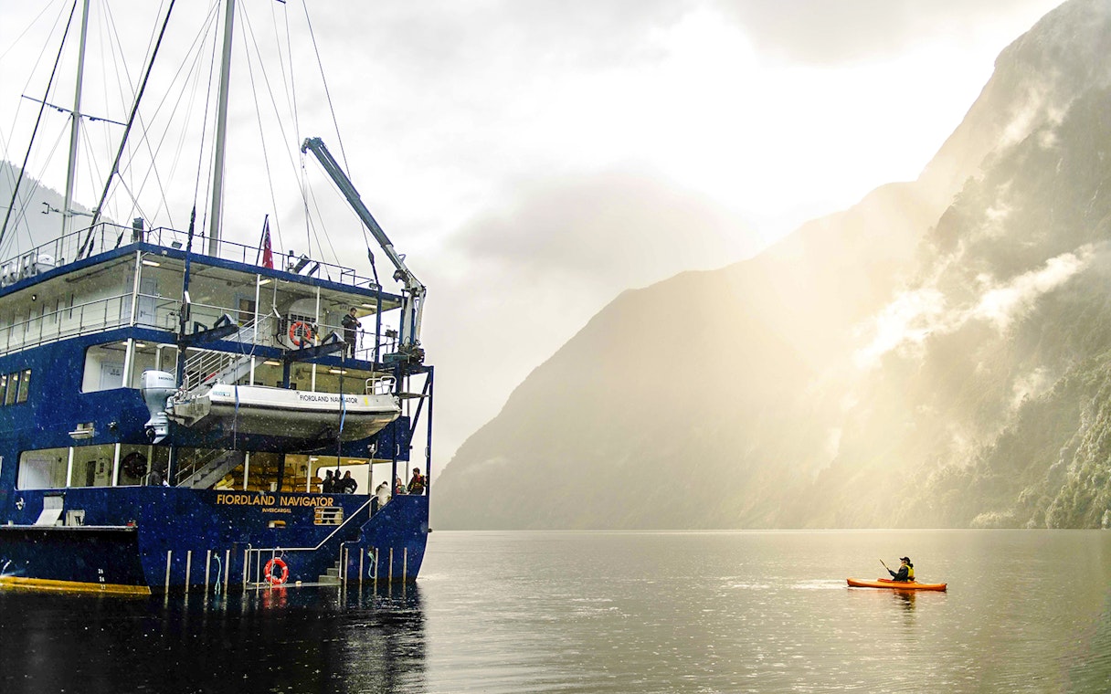 Kayaker paddling near a cruise ship in Doubtful Sound, New Zealand.