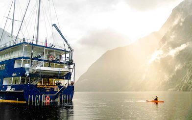 Kayaker paddling near a cruise ship in Doubtful Sound, New Zealand.