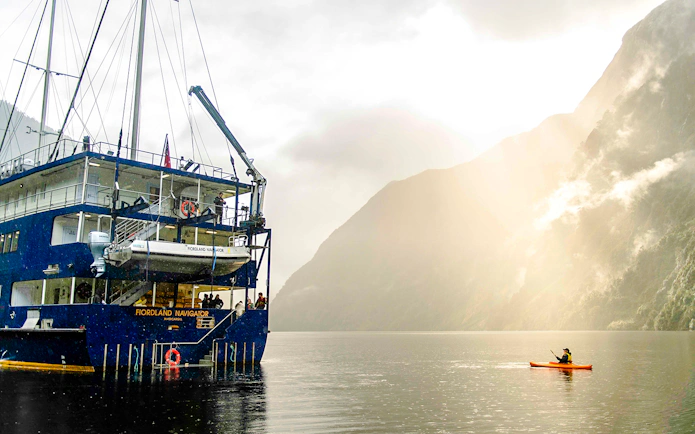 Kayaker paddling near a cruise ship in Doubtful Sound, New Zealand.