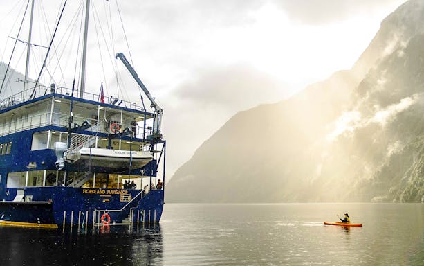 Kayaker paddling near a cruise ship in Doubtful Sound, New Zealand.