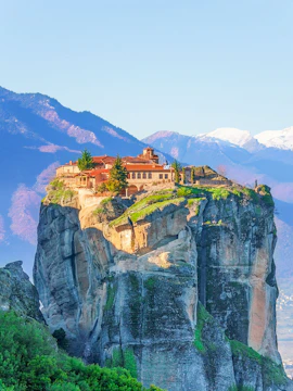 Monastery atop rock formation in Meteora, Greece, with mountains in the background.