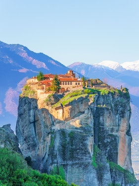 Monastery atop rock formation in Meteora, Greece, with mountains in the background.