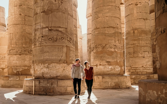 Couple exploring ancient columns at Luxor Temple, Egypt.