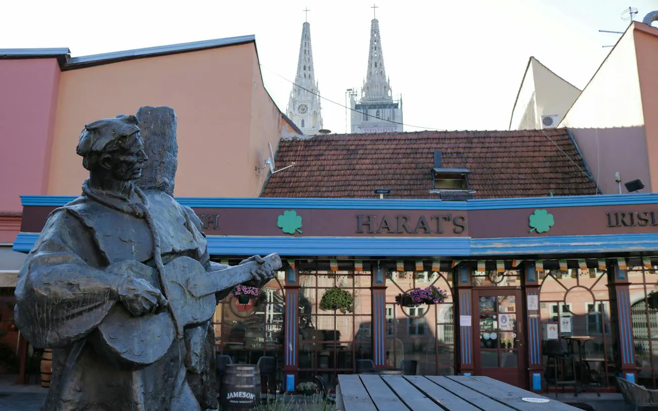 Statue of a musician in front of Harat's pub with Zagreb Cathedral spires in the background.