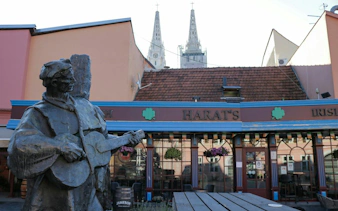 Statue of a musician in front of Harat's pub with Zagreb Cathedral spires in the background.