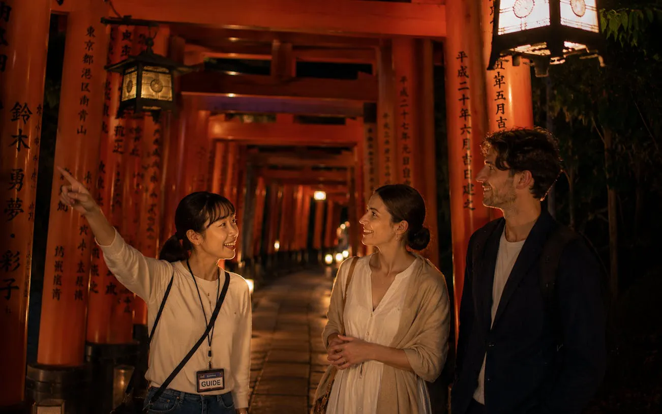 Guide leading a night tour through lantern-lit torii gates at Fushimi Inari, Kyoto.