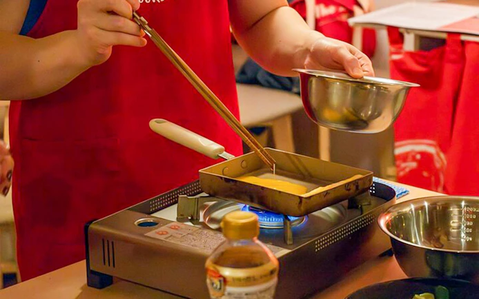 Cooking tamagoyaki on a stove during Tokyo izakaya-style evening class.