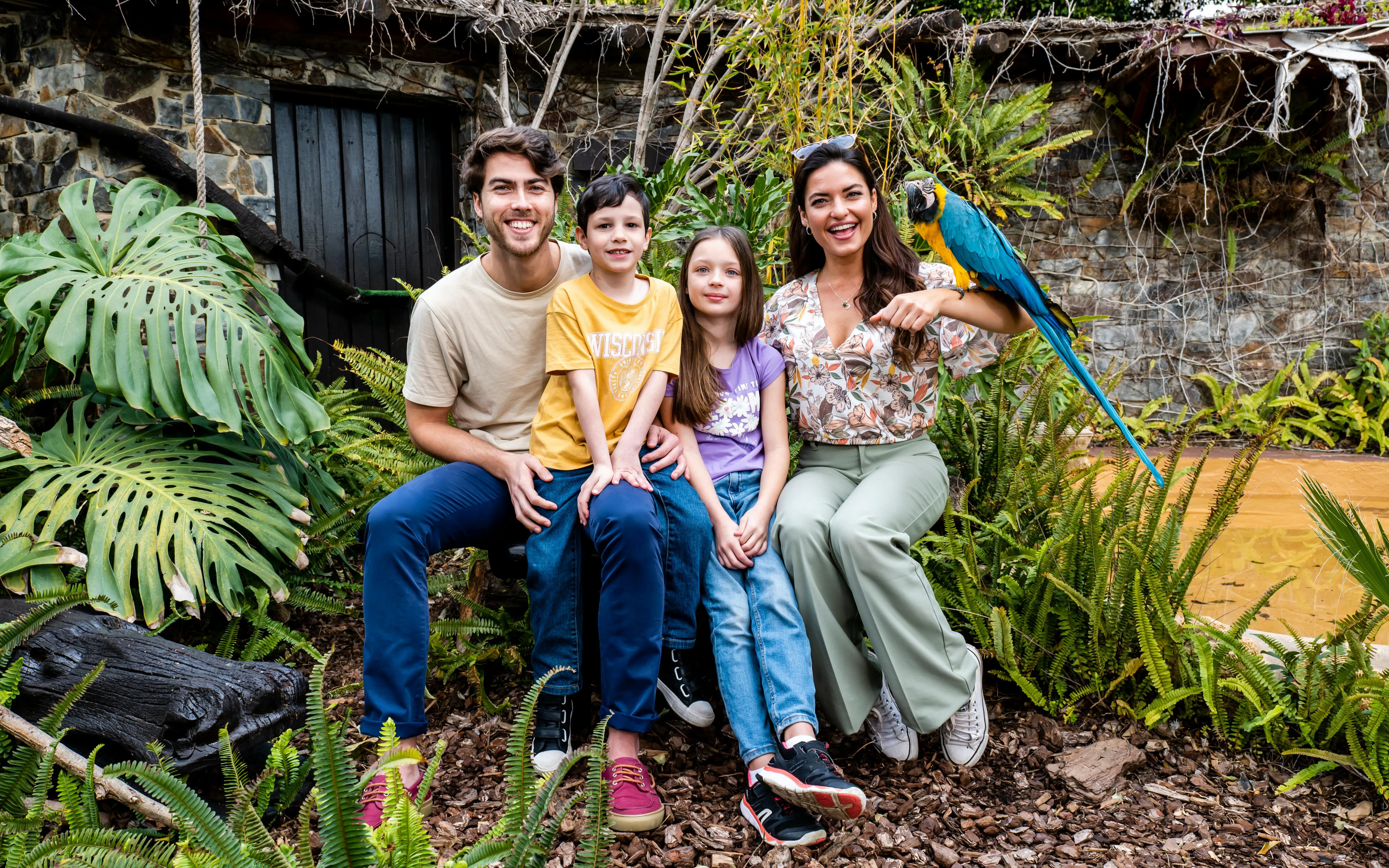 Family with a parrot at Selwo Marina Bird Center, surrounded by lush greenery.