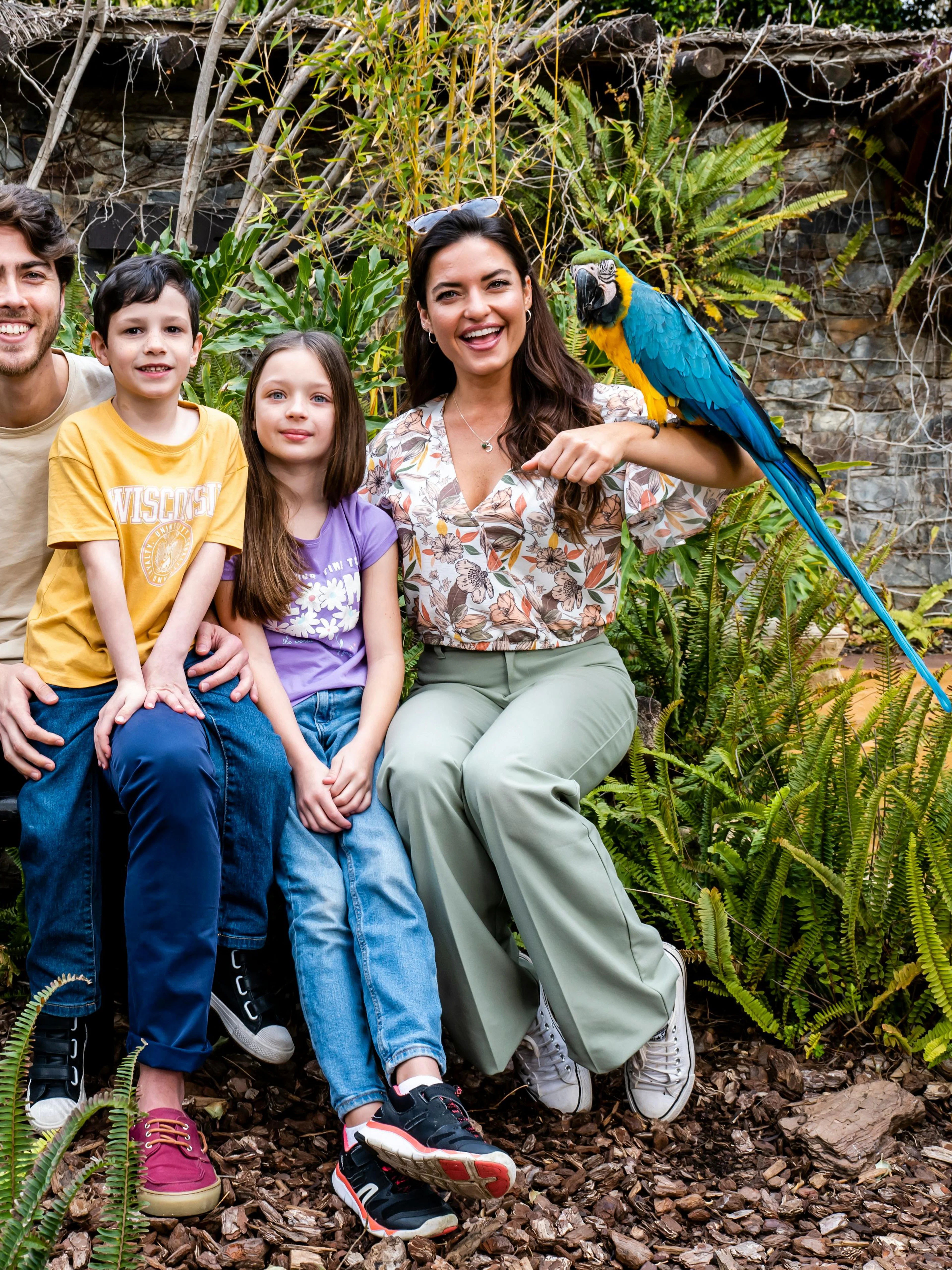 Family with a parrot at Selwo Marina Bird Center, surrounded by lush greenery.
