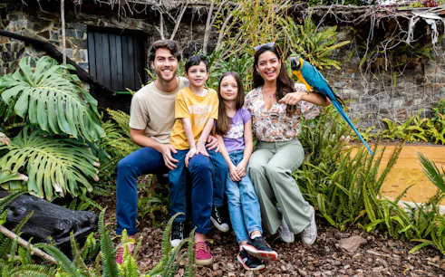 Family with a parrot at Selwo Marina Bird Center, surrounded by lush greenery.