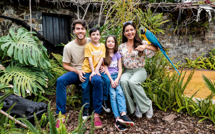 Family with a parrot at Selwo Marina Bird Center, surrounded by lush greenery.