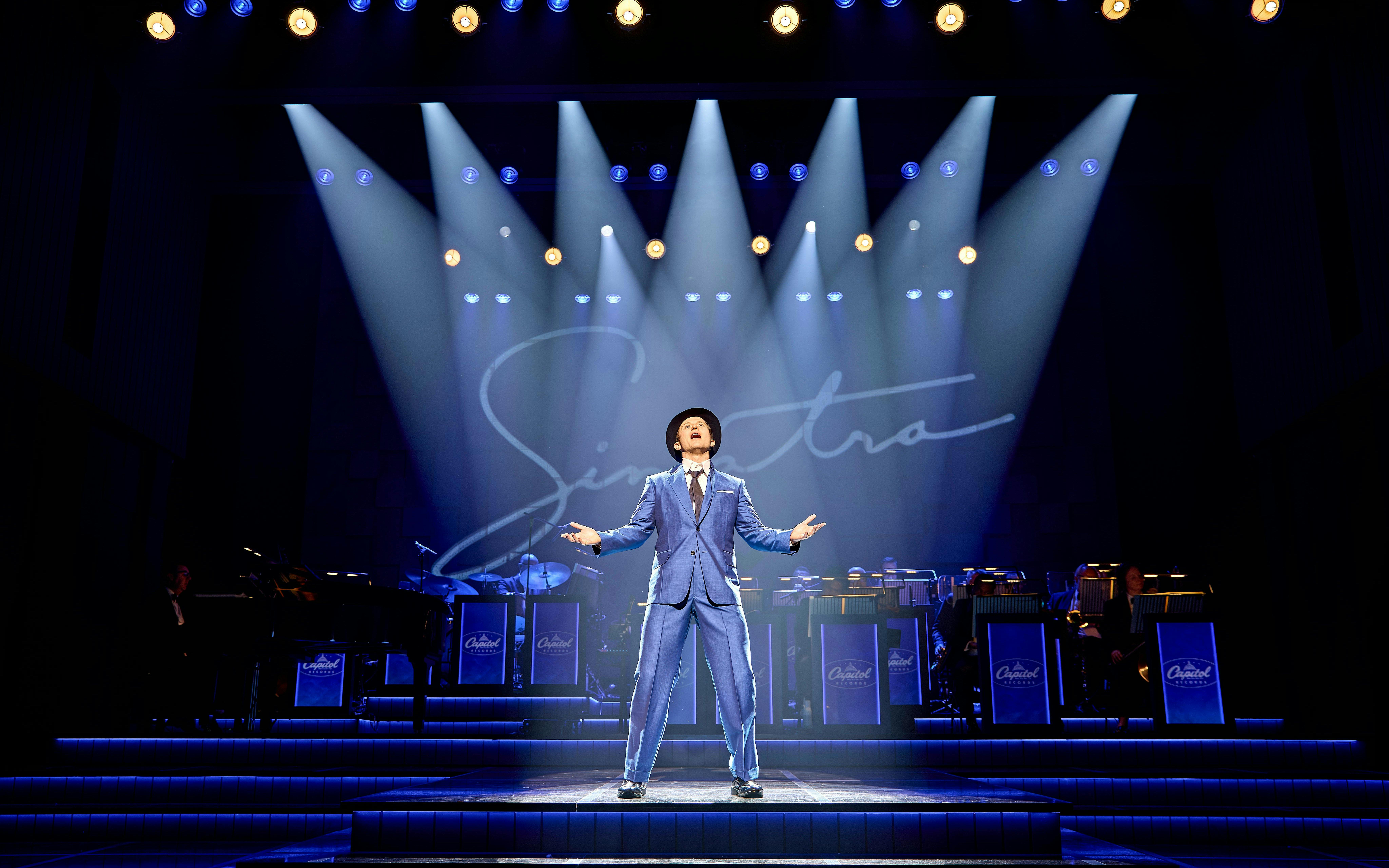 Performer on stage during Sinatra The Musical, Westend, with band and signature backdrop.
